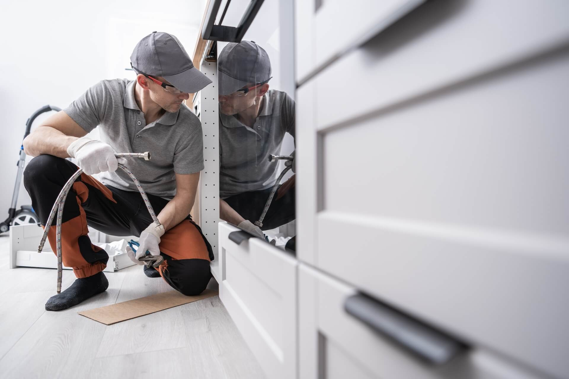 A fitter inspects the connections behind the kitchen cabinets, a detail work that is part of a thorough kitchen renovation.