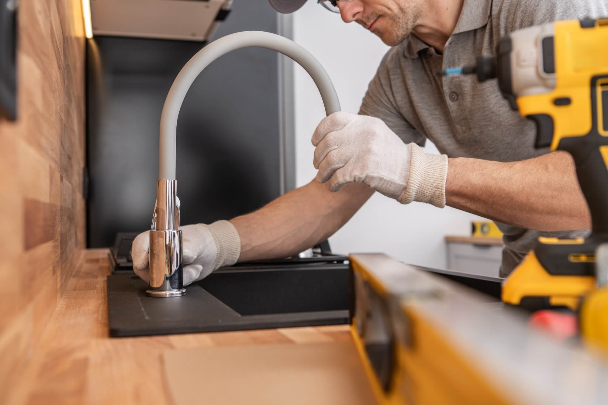 A plumber installs a new mixer tap in the kitchen, an important step in a complete kitchen renovation.